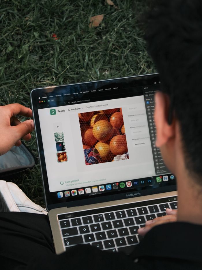 home-img A man sits outside on the grass and edits a fruit photo on a MacBook Pro.